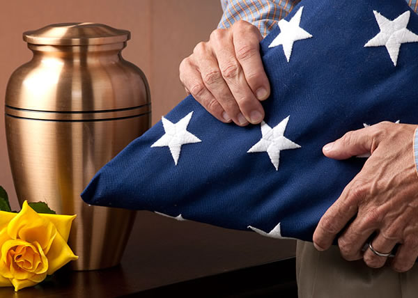 Veteran holding folded flag next to urn